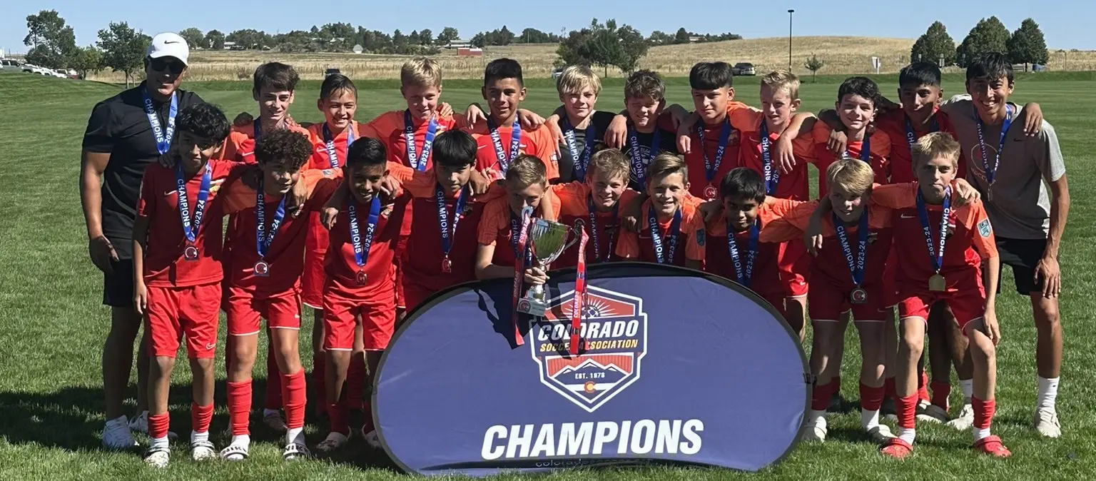 Real Colorado Academy team in red kits with Champions medals and trophy in front of Colorado Soccer Association Champions banner September 2023